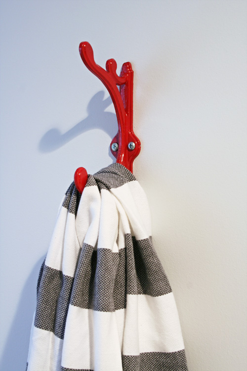 A grey and white towel hangs from a red hook.